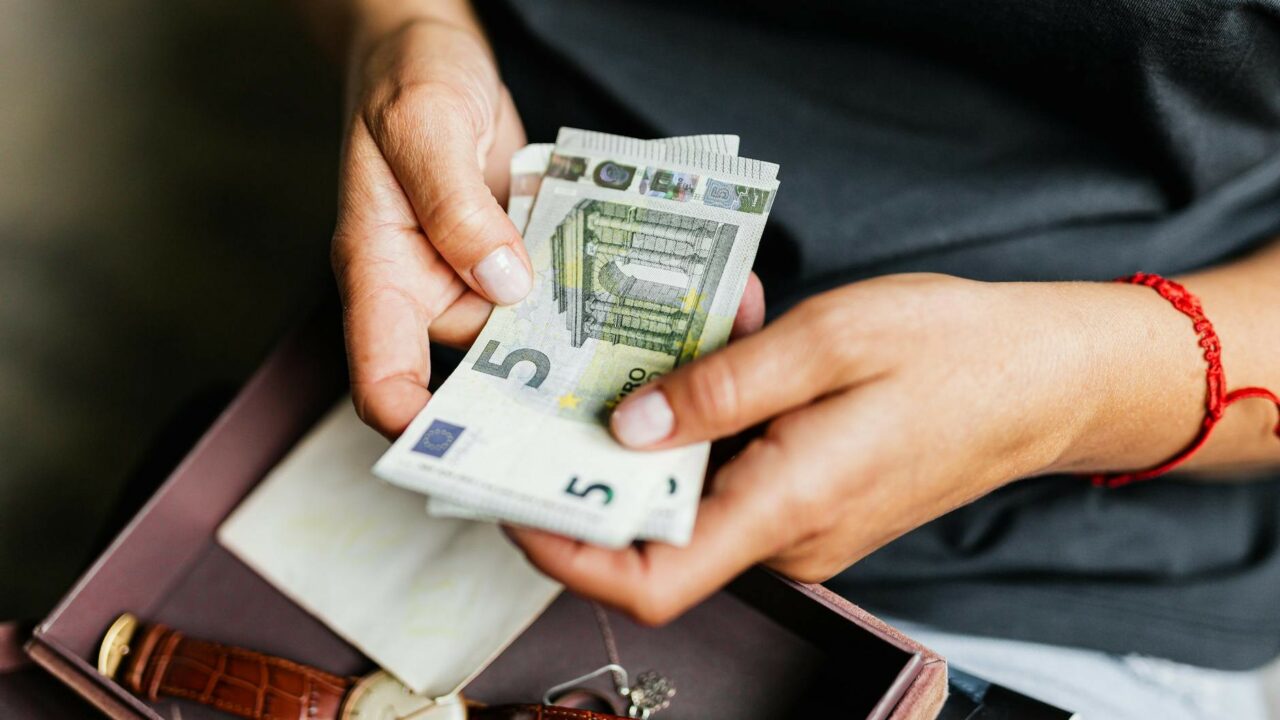 Mains comptant des billets en euros au-dessus d'une montre, illustration du compte à terme